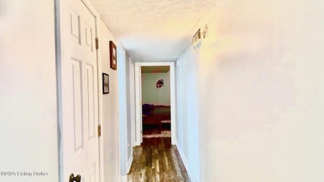 hallway featuring wood finished floors, baseboards, and a textured ceiling