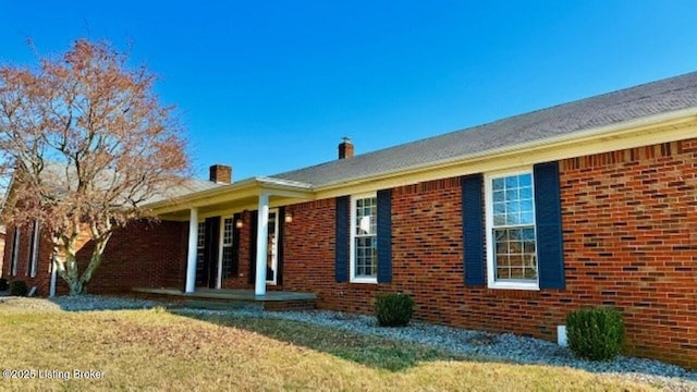 back of house with brick siding, covered porch, and a chimney