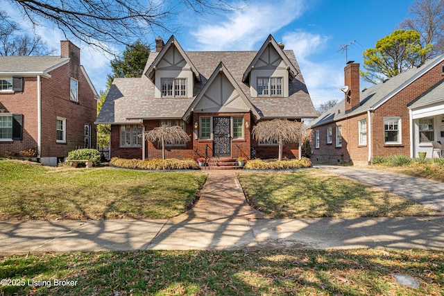 english style home with brick siding, a chimney, and a front lawn