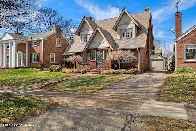 tudor house with driveway, stucco siding, an outdoor structure, a front lawn, and brick siding