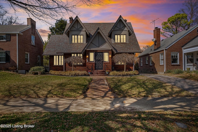 english style home with a front lawn, brick siding, and a chimney