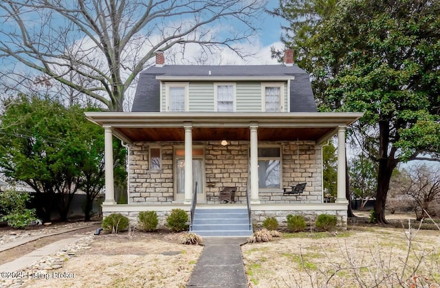 dutch colonial featuring stone siding, a porch, and a chimney