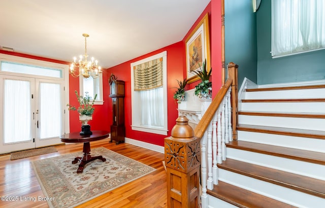 foyer featuring a healthy amount of sunlight, stairway, wood finished floors, and a chandelier