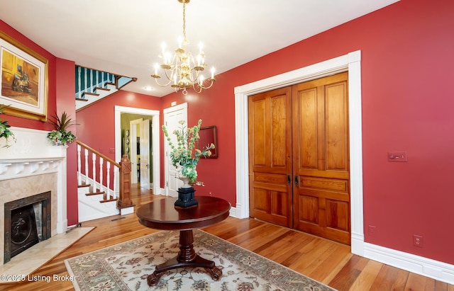 foyer with stairway, light wood-style floors, a fireplace, baseboards, and a chandelier