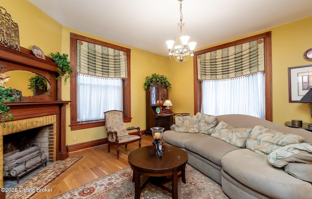 living room featuring a notable chandelier, a brick fireplace, baseboards, and wood finished floors