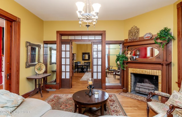 interior space with wood finished floors, baseboards, an inviting chandelier, french doors, and a brick fireplace