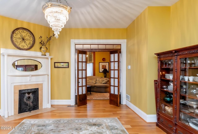 living area featuring visible vents, a fireplace, french doors, an inviting chandelier, and wood finished floors