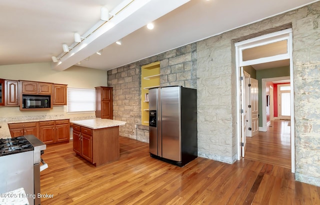 kitchen with a kitchen island, stainless steel fridge, black microwave, light wood finished floors, and vaulted ceiling with beams