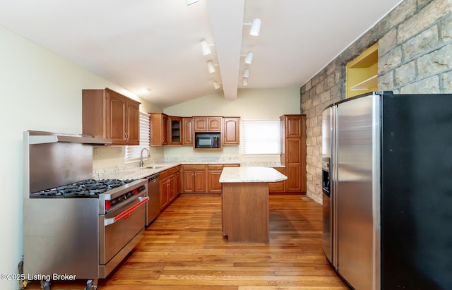 kitchen featuring light stone countertops, light wood finished floors, a sink, appliances with stainless steel finishes, and a center island