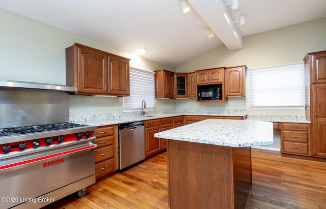 kitchen with lofted ceiling with beams, light stone counters, light wood-style floors, and appliances with stainless steel finishes