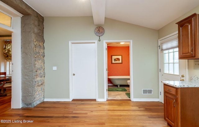 unfurnished dining area featuring visible vents, baseboards, light wood-style floors, and vaulted ceiling with beams