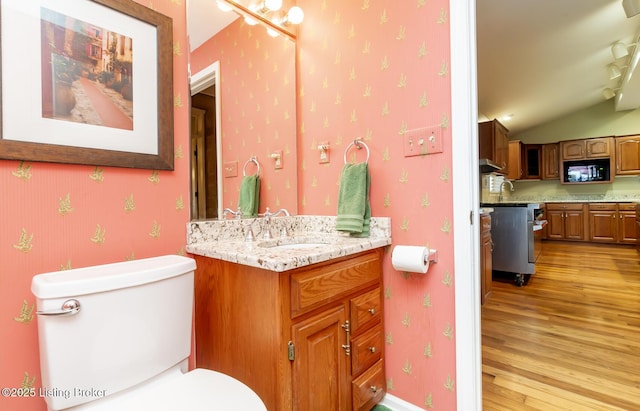 bathroom featuring vanity, wood finished floors, wallpapered walls, lofted ceiling, and toilet