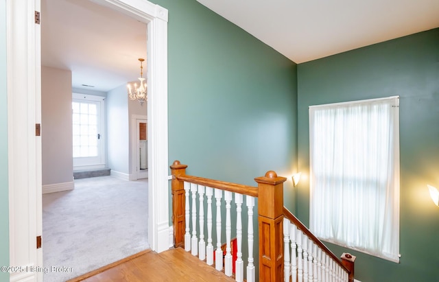 hall with an upstairs landing, a notable chandelier, wood finished floors, carpet, and baseboards