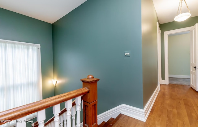 hall featuring an upstairs landing, light wood-style flooring, and baseboards