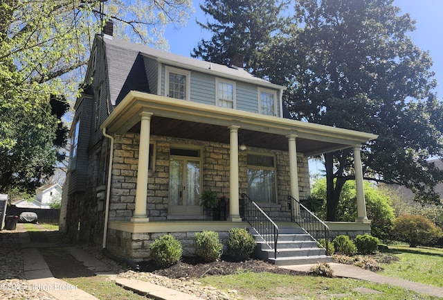 view of front facade featuring a porch, a chimney, and stone siding