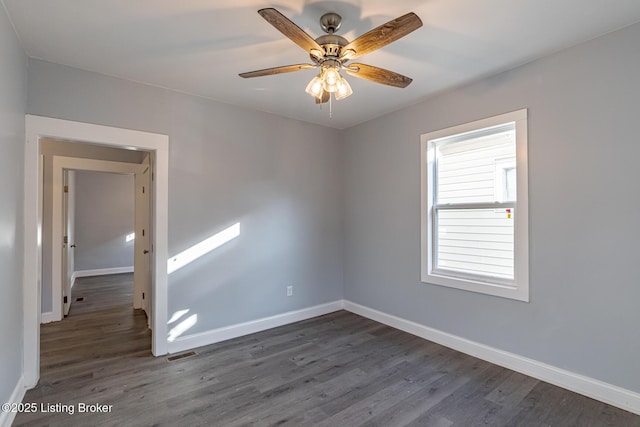 unfurnished room with dark wood-style floors, visible vents, ceiling fan, and baseboards