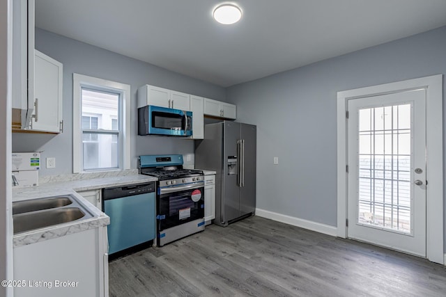 kitchen featuring light countertops, light wood-style floors, white cabinets, stainless steel appliances, and a sink