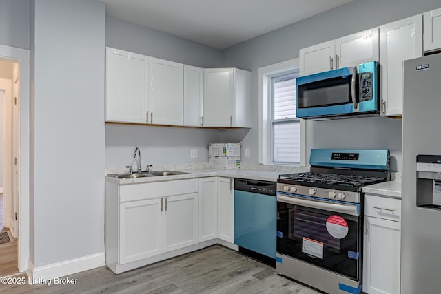 kitchen with light wood-style flooring, a sink, white cabinetry, stainless steel appliances, and light countertops