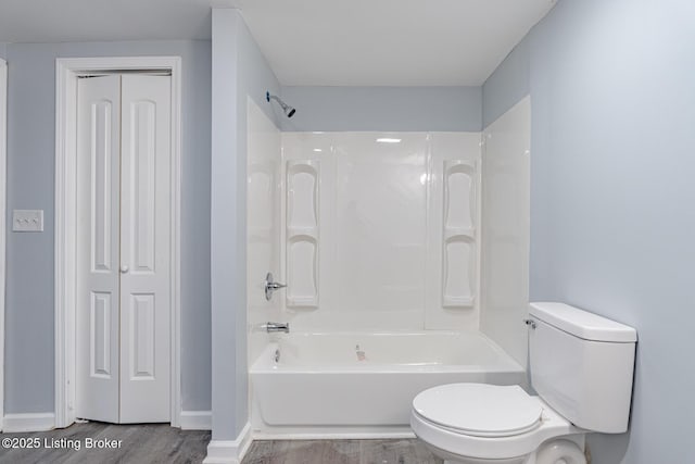 bathroom with wood finished floors, baseboards, tub / shower combination, a closet, and toilet