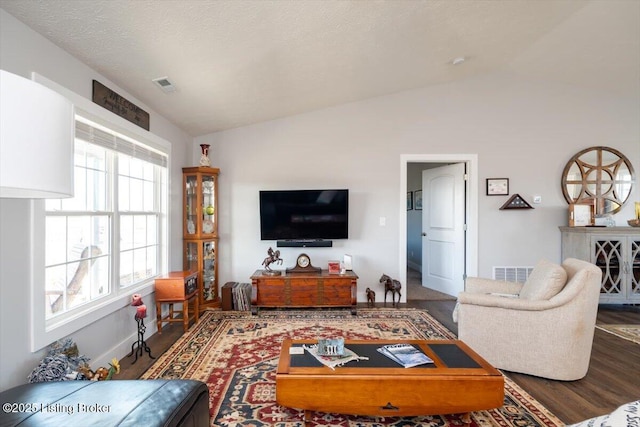 living area with vaulted ceiling, wood finished floors, visible vents, and a textured ceiling