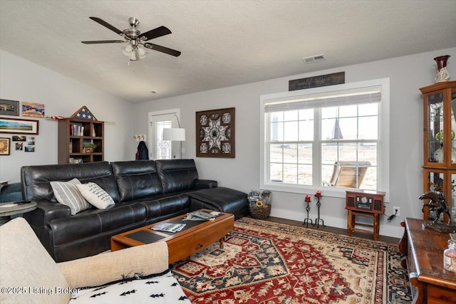 living room featuring a ceiling fan, visible vents, and a textured ceiling