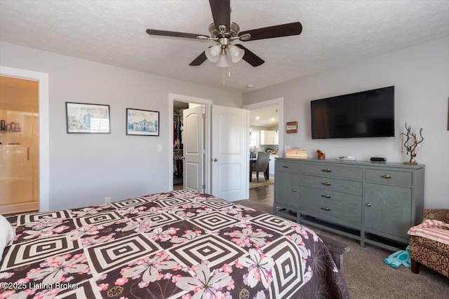 bedroom with a walk in closet, ceiling fan, dark carpet, ensuite bathroom, and a textured ceiling