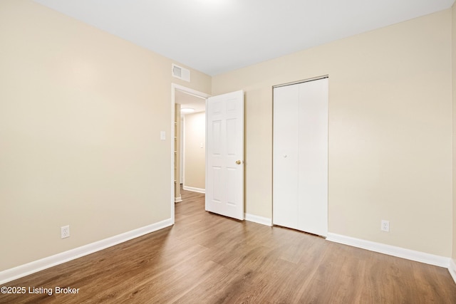 unfurnished bedroom with a closet, visible vents, baseboards, and wood finished floors