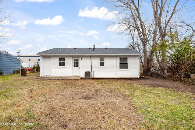 back of house with central AC unit, fence, a yard, and roof with shingles