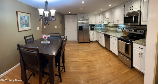 kitchen with backsplash, light stone counters, light wood-style flooring, appliances with stainless steel finishes, and a sink