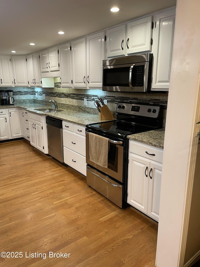 kitchen with light wood finished floors, a sink, appliances with stainless steel finishes, white cabinetry, and backsplash