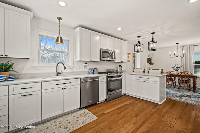 kitchen featuring light wood-style flooring, a sink, white cabinetry, a peninsula, and appliances with stainless steel finishes