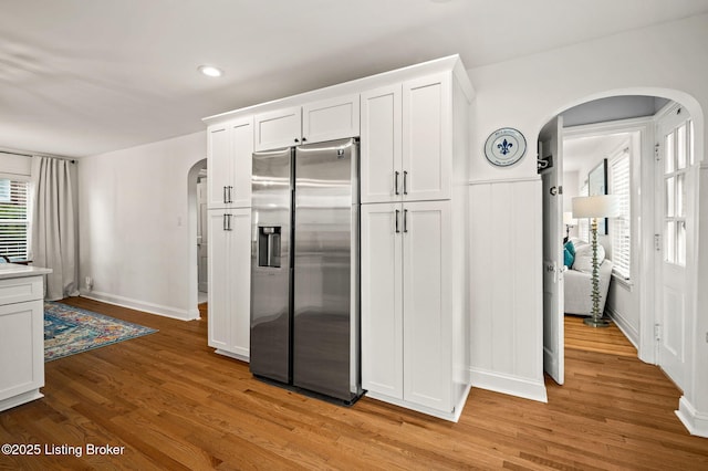 kitchen with light wood-style flooring, stainless steel fridge with ice dispenser, arched walkways, light countertops, and white cabinetry