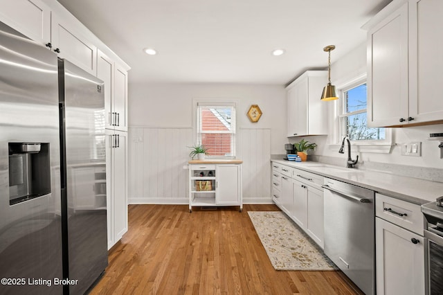 kitchen featuring a wainscoted wall, a sink, light wood-style floors, appliances with stainless steel finishes, and white cabinetry