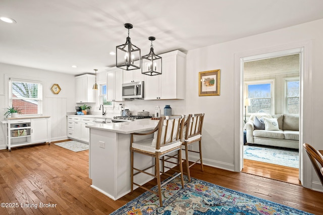 kitchen with light wood-type flooring, stainless steel microwave, range, and a peninsula