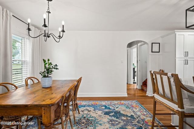 dining space featuring baseboards, wood finished floors, arched walkways, and a chandelier