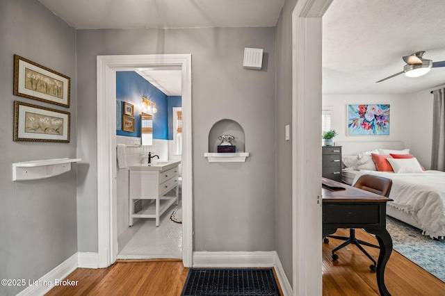 bedroom featuring wood finished floors, baseboards, ensuite bathroom, and a sink