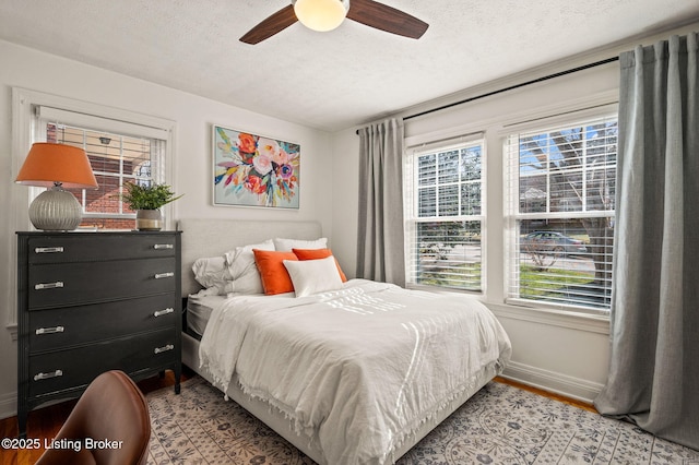 bedroom with ceiling fan, wood finished floors, baseboards, and a textured ceiling