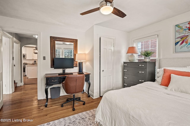 bedroom featuring wood finished floors, arched walkways, and ceiling fan