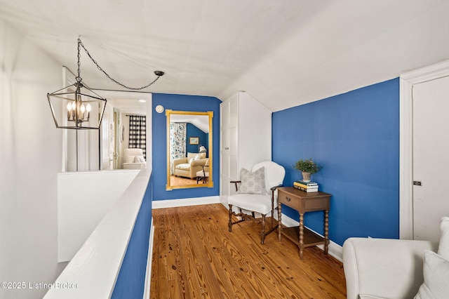 living area with baseboards, an inviting chandelier, wood finished floors, and vaulted ceiling