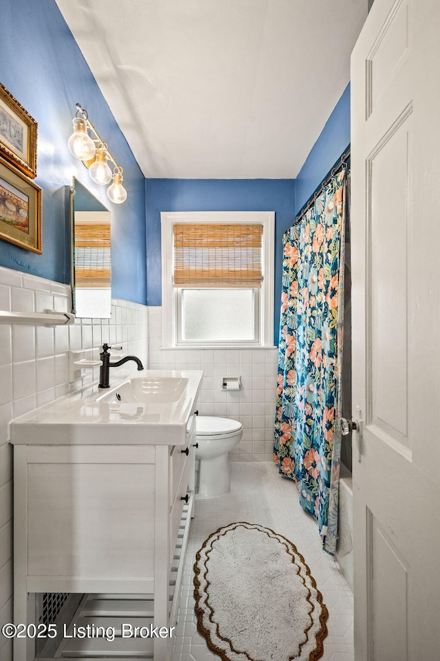 bathroom featuring tile patterned floors, toilet, tile walls, wainscoting, and vanity