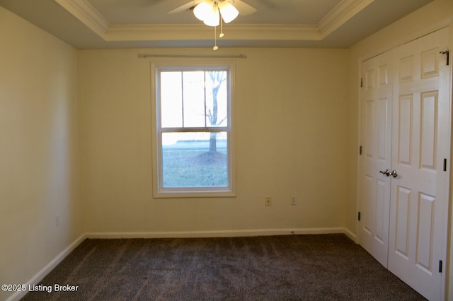 unfurnished room with a tray ceiling, dark carpet, and crown molding