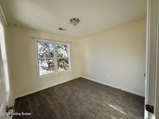 spare room featuring baseboards, visible vents, and dark carpet