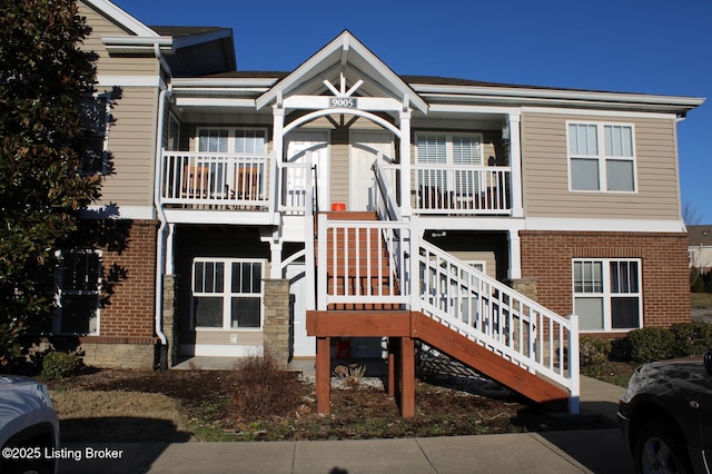 view of front of house featuring stairs, covered porch, and brick siding