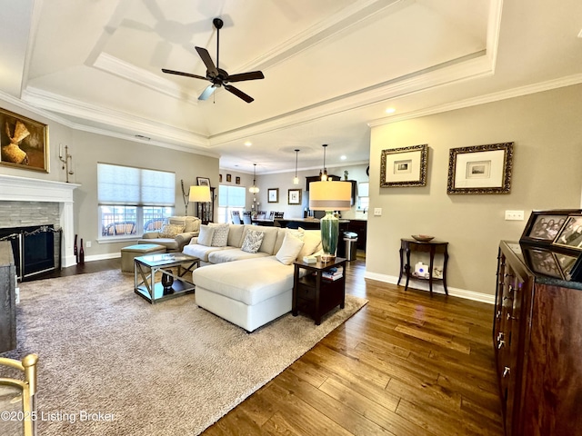 living room featuring crown molding, baseboards, a stone fireplace, dark wood-style floors, and a raised ceiling