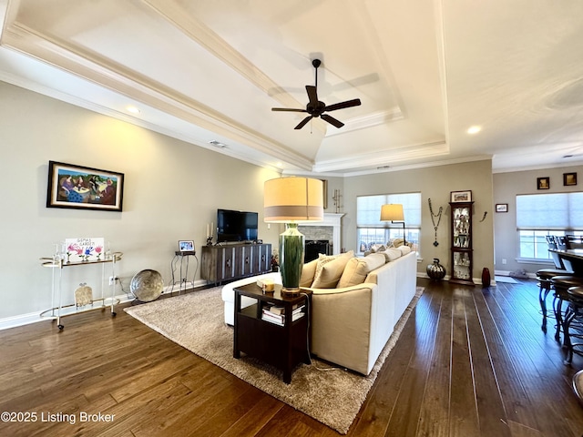 living area featuring baseboards, dark wood finished floors, a tray ceiling, a fireplace, and crown molding