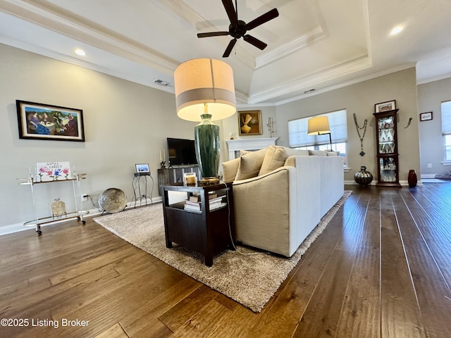 living room featuring visible vents, ornamental molding, a ceiling fan, a tray ceiling, and dark wood finished floors