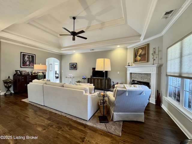 living room featuring visible vents, crown molding, dark wood finished floors, a fireplace, and arched walkways