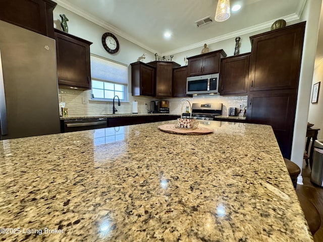 kitchen with visible vents, light stone countertops, ornamental molding, decorative backsplash, and appliances with stainless steel finishes