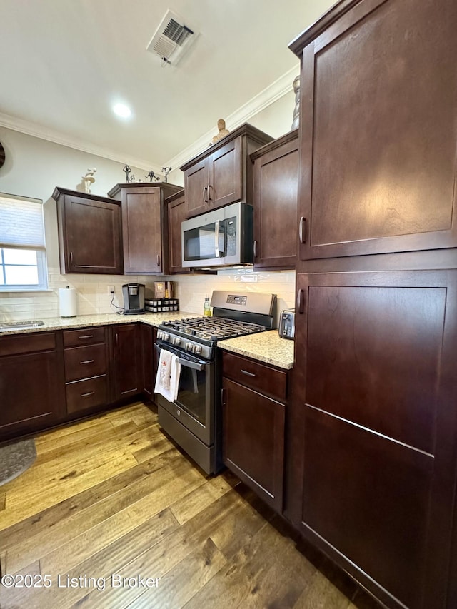 kitchen featuring visible vents, light wood-style flooring, stainless steel appliances, crown molding, and tasteful backsplash