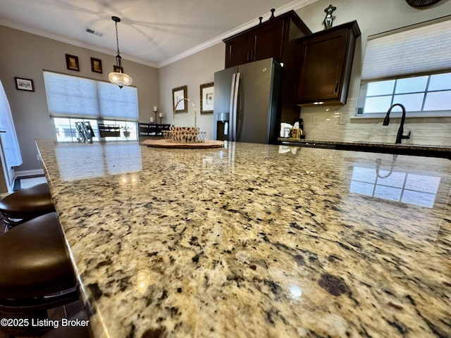 kitchen featuring a breakfast bar area, light stone counters, ornamental molding, dark brown cabinets, and stainless steel refrigerator with ice dispenser